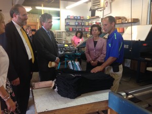 Nelson Silva shows Gov. Raimondo, Lieutenant Gov. McKee, and Sec. Pryor shirts made by his staff.